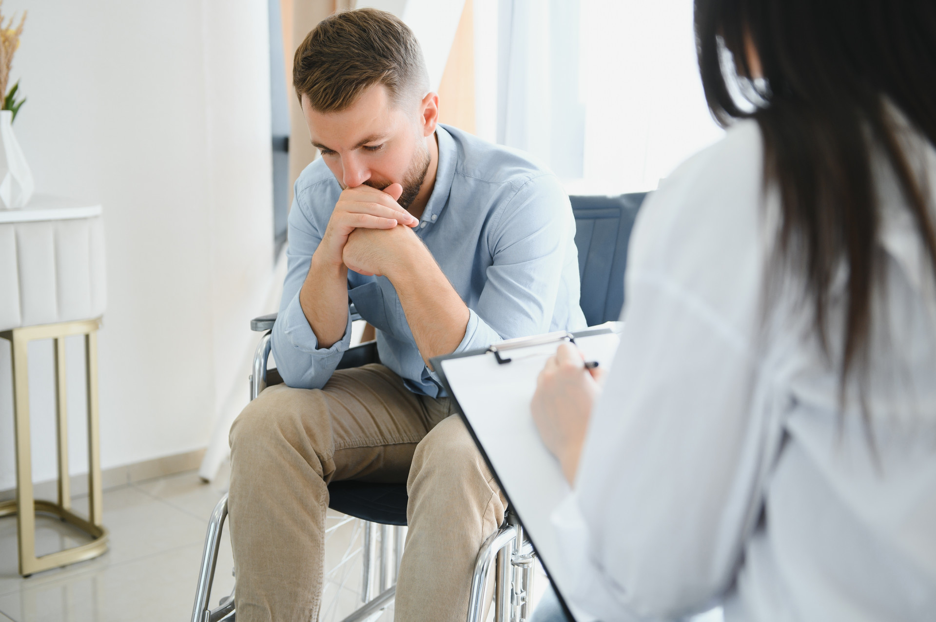 Man in wheelchair with head in hands during counseling session