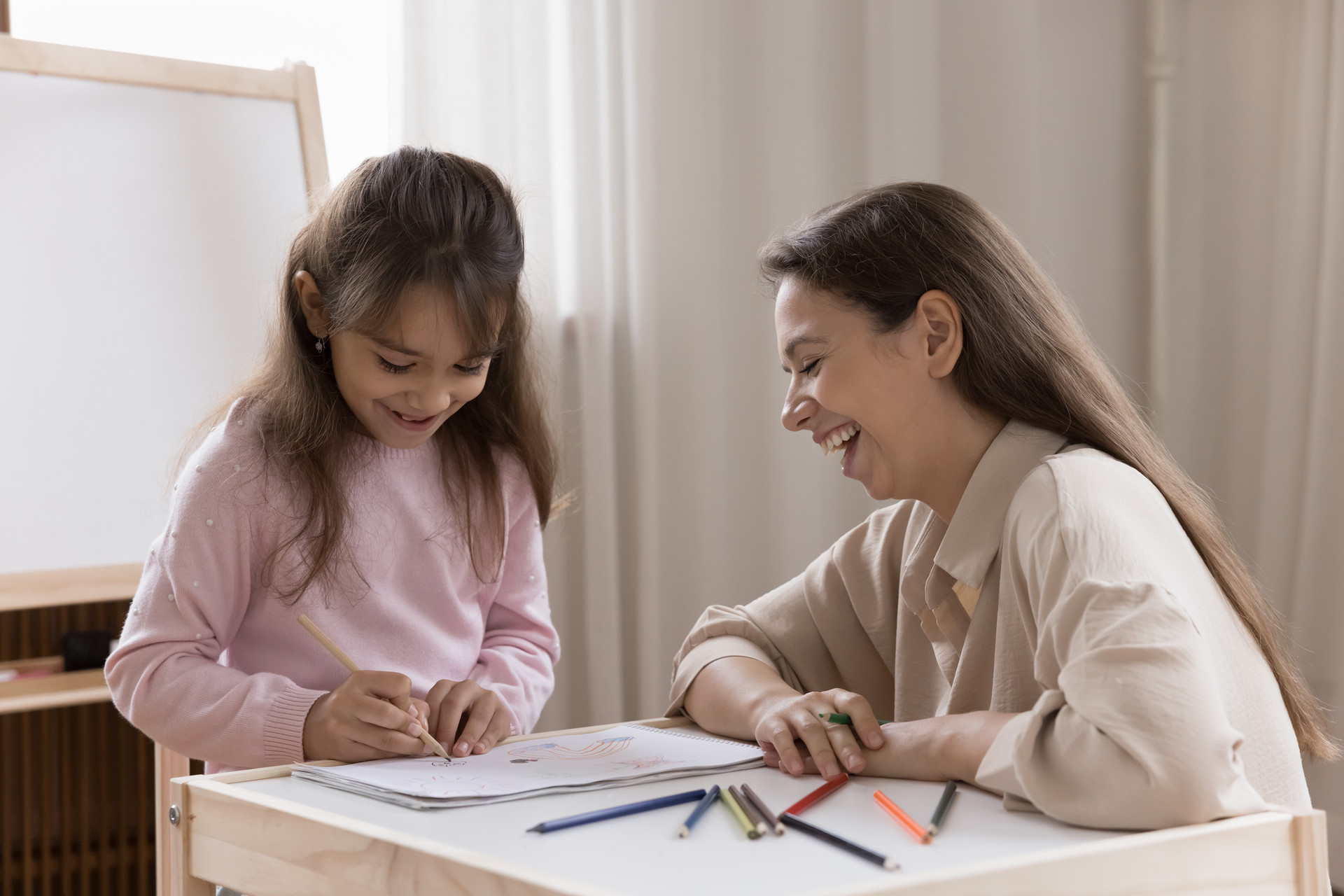 Counselor doing art therapy with child. Child is drawing on paper with colored pencils.