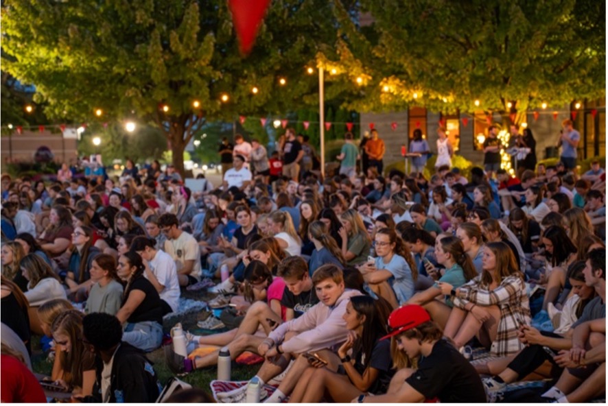 Large group of students (100+) sitting outside on the grass